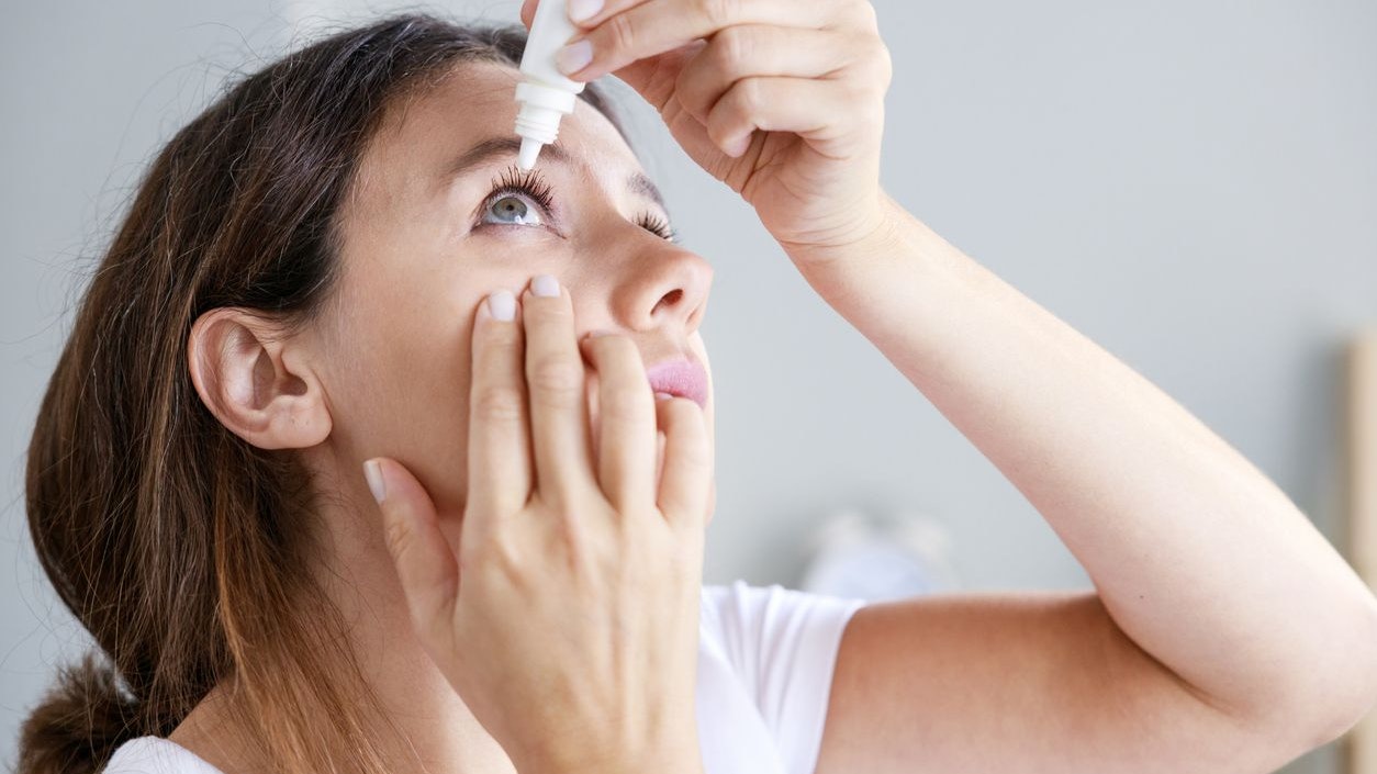 Young woman putting eye drops at home