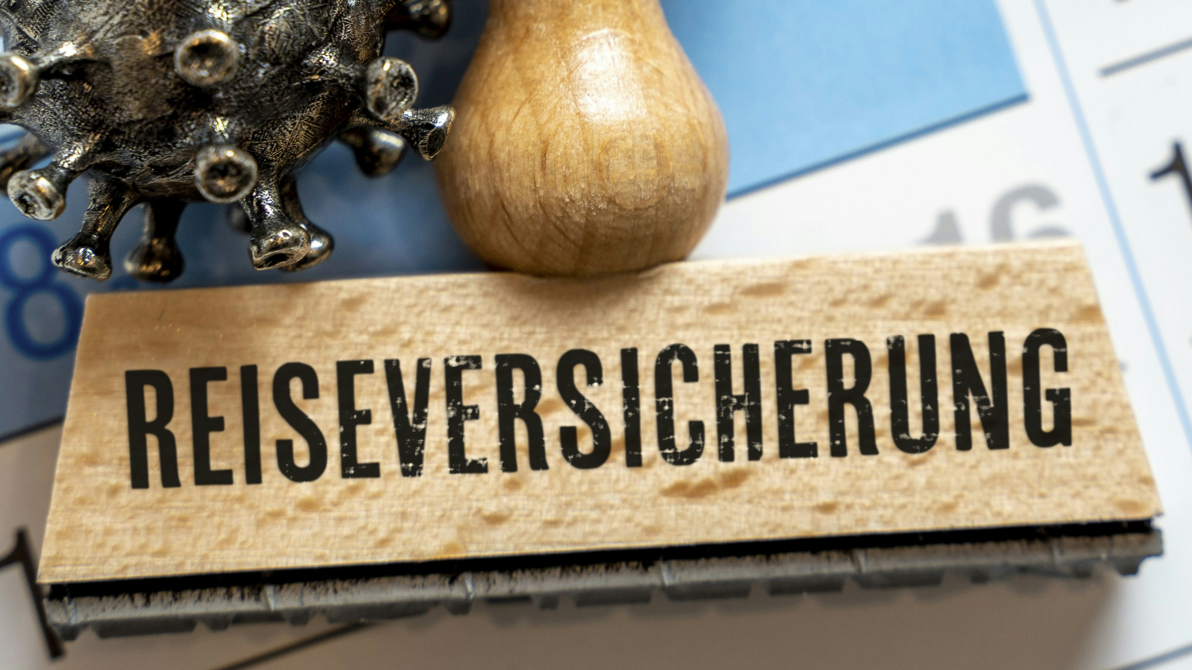 Download von www.picturedesk.com am 22.10.2025 (10:50).  Symbolbild Reiseversicherung. Stempel auf einem Kalender mit Virusfigur und eingetragenen Krankheitstagen im Kalender FOTOMONTAGE - 20230731_PD3451 - Rechteinfo: Rights Managed (RM)